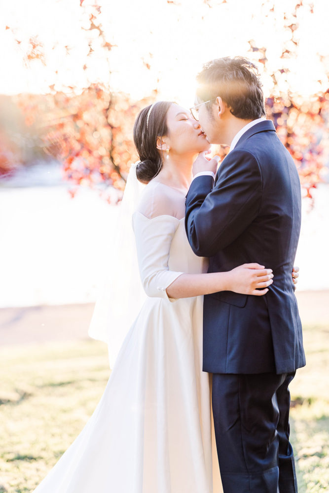 bride and groom sharing a sweet kiss at sunset among fall leaves and a lake behind